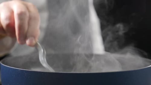 White Smoke in Slow Motion Rising Above Hot Frying Pan on Black Background Preparing Meal Stirring