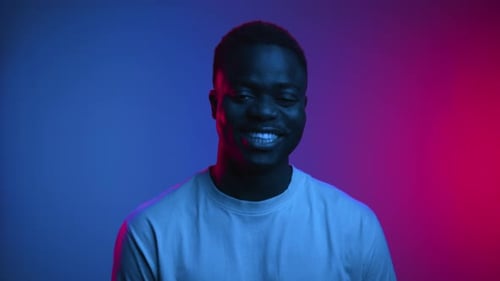 Happy Portrait of Black Man Face Looking at Camera and Smiling in Neon Studio