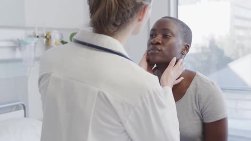 Diverse female patient and doctor checking her neck with hands in hospital, in slow motion