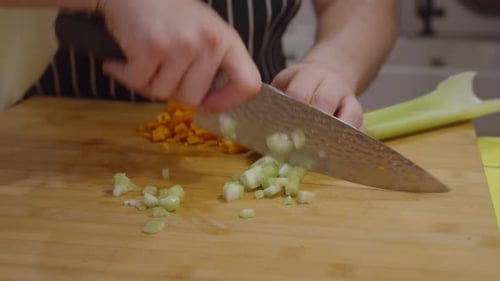 Der Koch schneidet Selleriegemüse auf einem Holzschneidebrett. Nahaufnahme der Hände. Zeitlupe.
