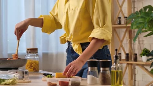 Woman Cooking Pasta and Cutting Cheese in Kitchen