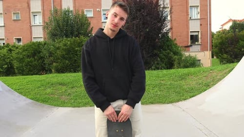 Camera Approaching a Skater Posing with His Skateboard at the Skate park
