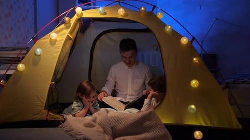 Man Reading Book to Children in Tent at Night