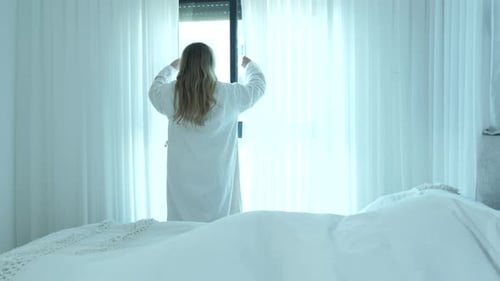 Beautiful young blonde woman open and close curtain in bedroom in the morning