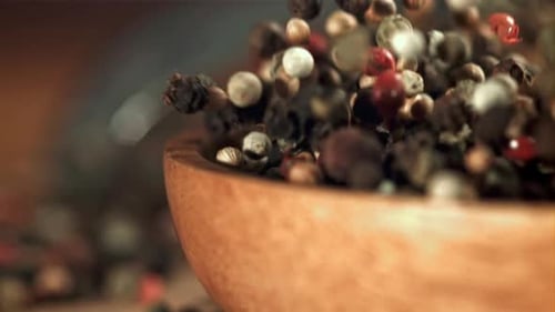 Peppercorns Falling into a Wooden Bowl Close Up