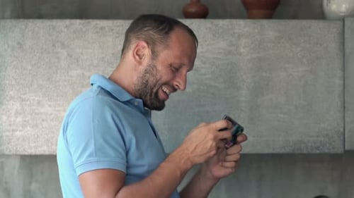 Man Smiling and Using Smartphone in Kitchen