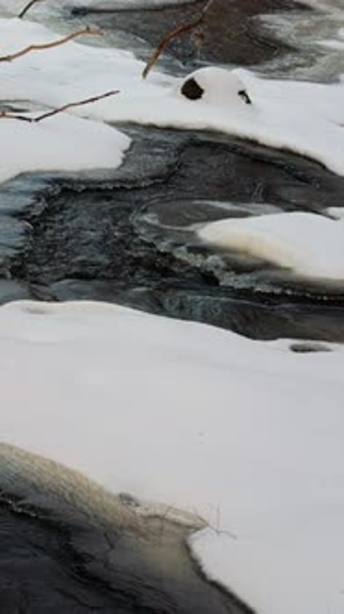 Ruisseau partiellement gelé entouré de neige, de l'hiver au printemps