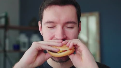 Young caucasian man bites into burger, burger eating pleasure, close up portrait fast food eating, u