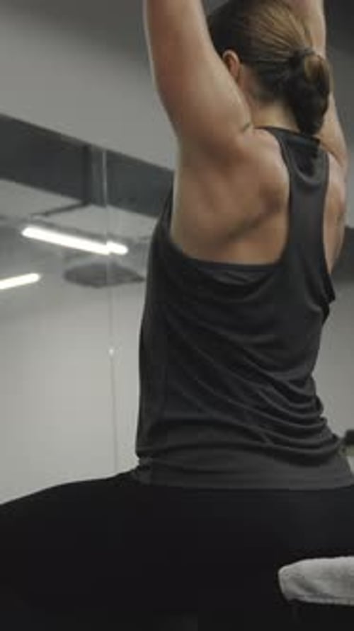 Vertikales Video. Junge Frau sitzt auf einer Bank im Fitnessstudio, beim Hantelheben, vor einem Spiegel
,.