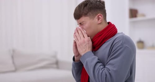 Young man with runny nose sneezing at home. Cold symptom