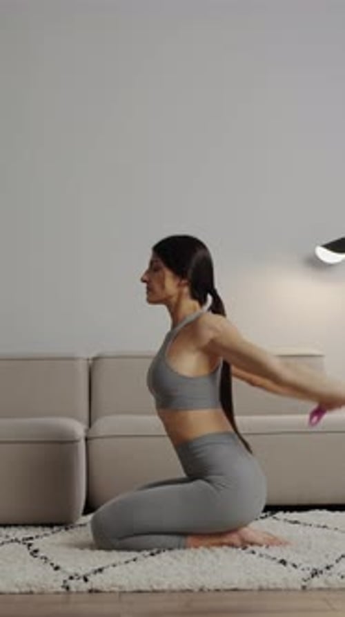 Focused Woman in Gray Activewear Practicing Seated Home Workout with Pink Dumbbells on Soft Rug