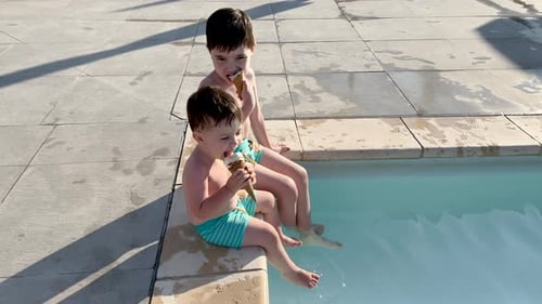 adorable kids siblings brothers on pool edge eating cone ice cream,legs feet playing into water wave