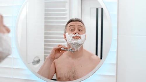 Adult Man Shaving in Bright Bathroom Mirror