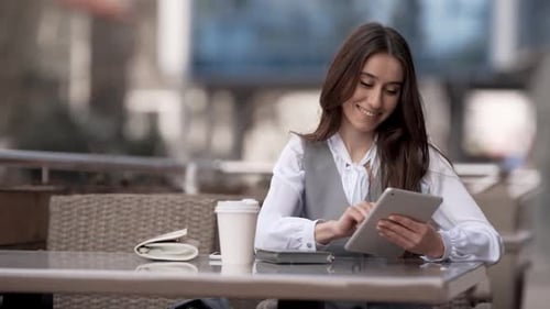 Young business woman sitting on summer terrace of cafe with tablet smiling