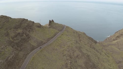 Panorama drone shot of a car driving through a road in the mountains and ocean in the background