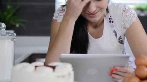 Cheerful brunette woman enjoys baking with a tablet computer in her kitchen