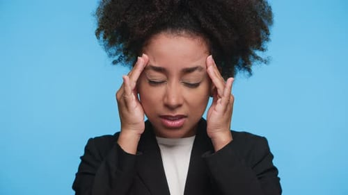 Woman Massaging Forehead in Distress on Blue Background