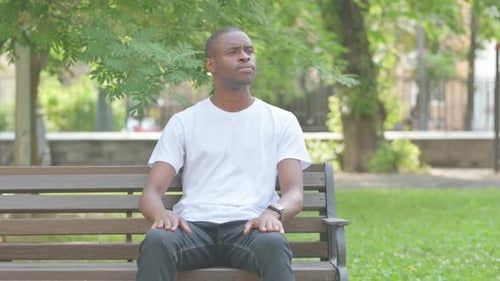African American Man Checking Time while Sitting on Bench in Park
