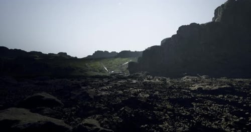 Lush Valley with Rocky Terrain and Distant Waterfall Under Sunlight