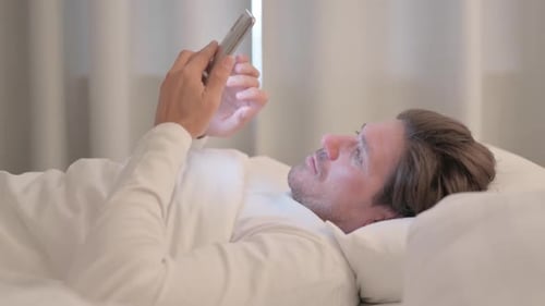 Side View of Mature Adult Man Upset by Loss on Phone in Bed