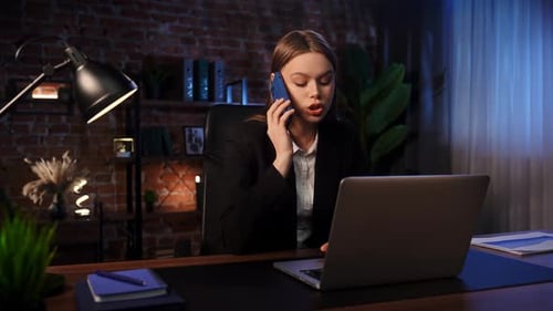 Businesswoman in Office Talking on Phone and Using Laptop