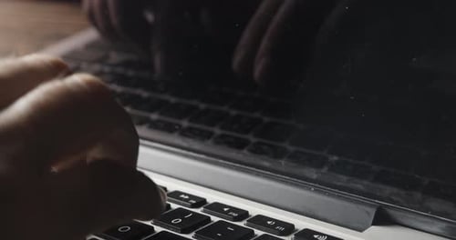 Hand Typing on Laptop Keyboard with Reflection Mirrored in Screen
