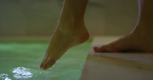 Nahaufnahme der Füße einer jungen Frau beim Betreten einer Whirlpool-Badewanne in einem luxuriösen Wellnesscenter.