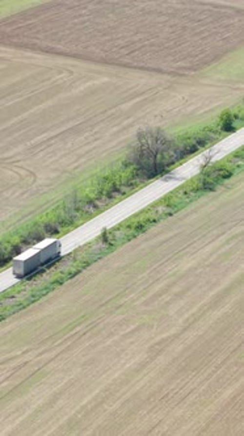 Aerial Drone View of Delivery Truck Driving on Highway Surrounded By Open Fields