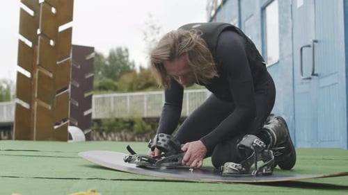 Man Preparing Wakeboard Outdoors on Green Surface