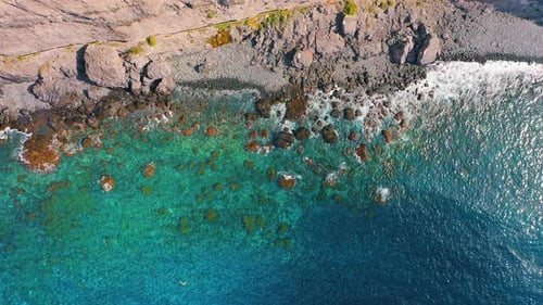 Top Down Aerial View From Above Ocean Waves Crashing and Foaming on Empty Rocky Tropical Beach with