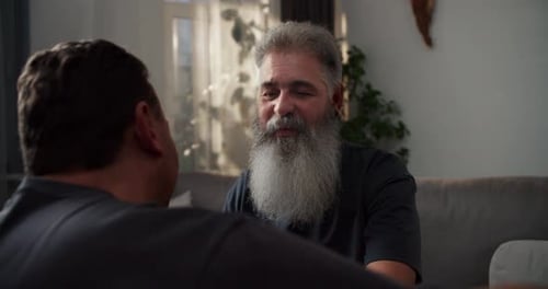Close Up Over the Shoulder of a Happy Man with Gray Hair and a Lush Gray Beard Hugging His Brunette
