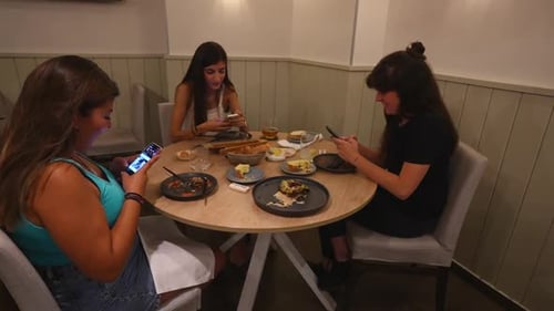 Three women at a cafe using smartphones during a meal