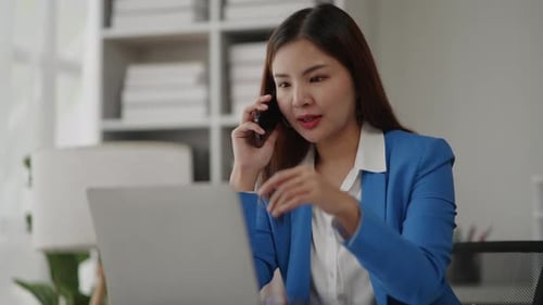 Woman Talks on Phone at Laptop in Office