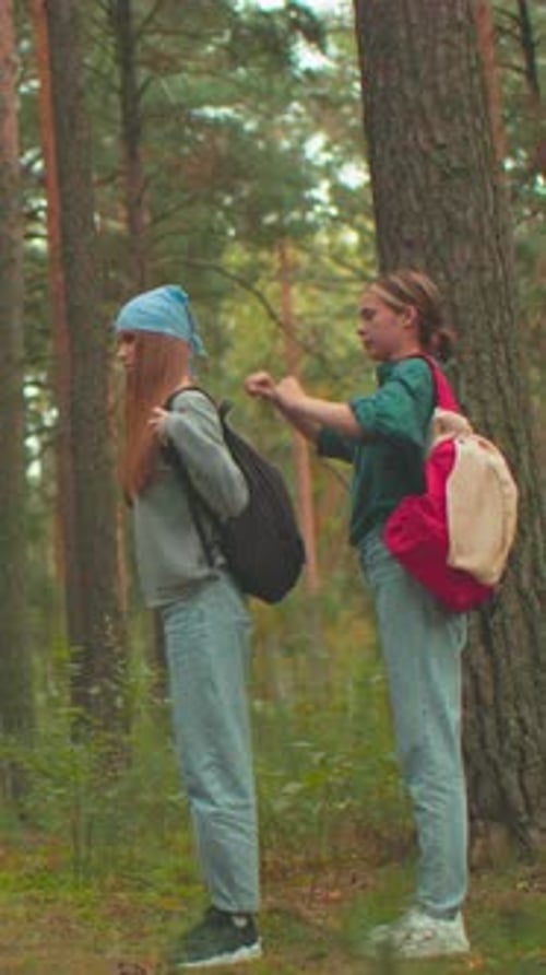 Two Women Share Moment in Forest Helping Each Other with Backpacks
