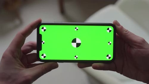 hands holding smartphone with green screen display and tracking markers, changing orientation from p