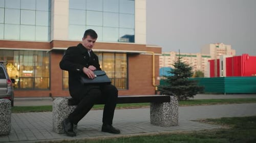 Businessman in Black Coat Trying to Open Briefcase Outdoors in Urban Setting