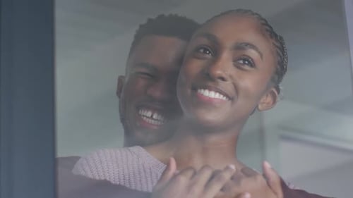 Close up of happy african american couple standing at window and hugging