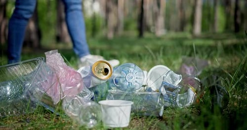 A Woman Walks Past a Pile of Garbage in the Forest and Throws a Glass Bottle at It