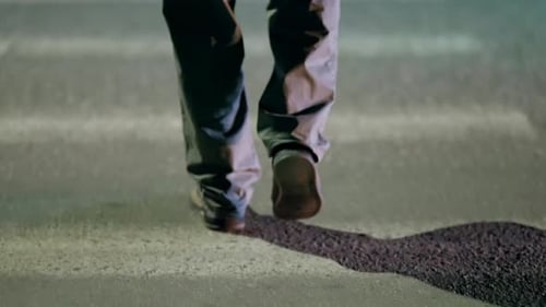 Closeup View of a Pedestrian Walking Across a Dimly Lit Crosswalk at Night Showcasing Legs and Feet