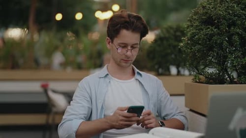 Young Man Using Smartphone While Studying at Outdoor Cafe