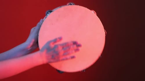 Woman Plays Tambourine Against Red Background in Studio