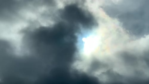 La lumière du soleil perce à travers de sombres nuages inquiétants créant des couleurs irisées autour du soleil.