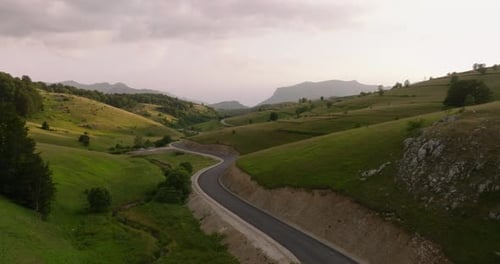 Winding road through rolling green hills and mountains under a cloudy sky