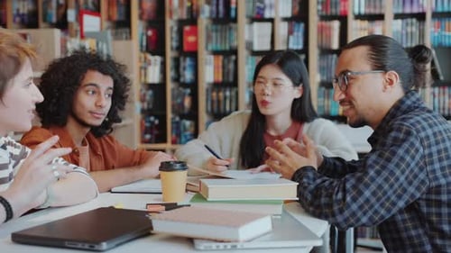 Group of Diverse College Students Discussing Homework in Library