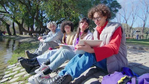 College Students Sitting by Pond in the Park and Discussing Homework