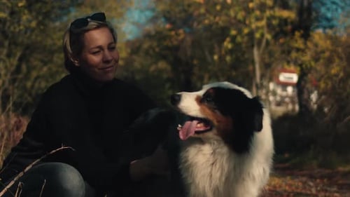 Woman smiles as she pets dog in field on autumn day