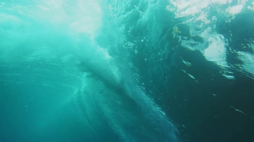 Unterwasser-Rückansicht eines Surfers, der eine steile Welle gegen ein Fass fängt
