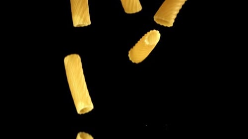Rigatoni pasta falling on a reflective black surface