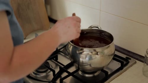 Weibliche Hände rühren die Marmelade mit einem Holzlöffel um. Der Prozess der Herstellung von Aprikosenmarmelade
.