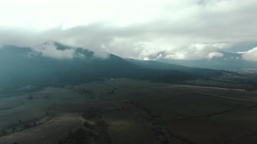 Dramatic Drone Footage of a Vast Field and Majestic Mountain Beneath a Cloudy Sky